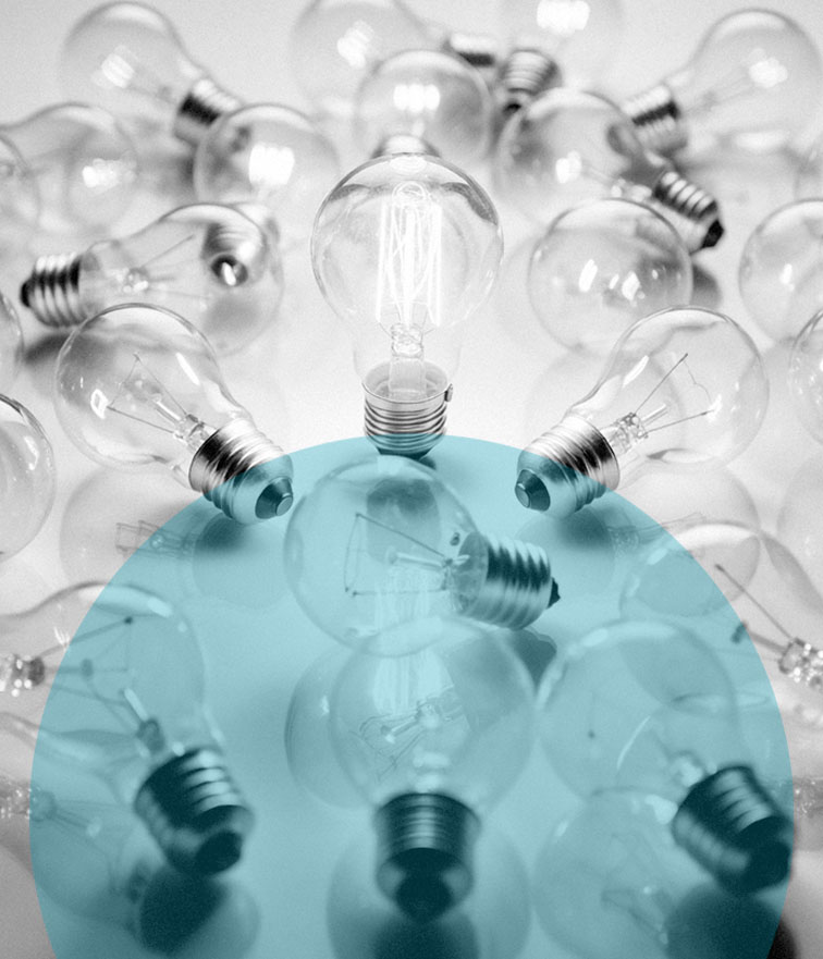 Schwarz-weißes Foto, das wie eine Metapher für einen kognitiven Leistungstest im Rahmen von Personalauswahl wirkt: Zahlreiche Glühbirnen liegen verstreut auf einer reflektierenden Oberfläche. Im Zentrum steht eine einzelne, strahlend leuchtende Edison-Glühbirne, die kognitive Höchstleistung oder den bzw. die beste*n Bewerber*in symbolisiert. Sie überragt die umliegenden, größtenteils unbeleuchteten Glühbirnen.